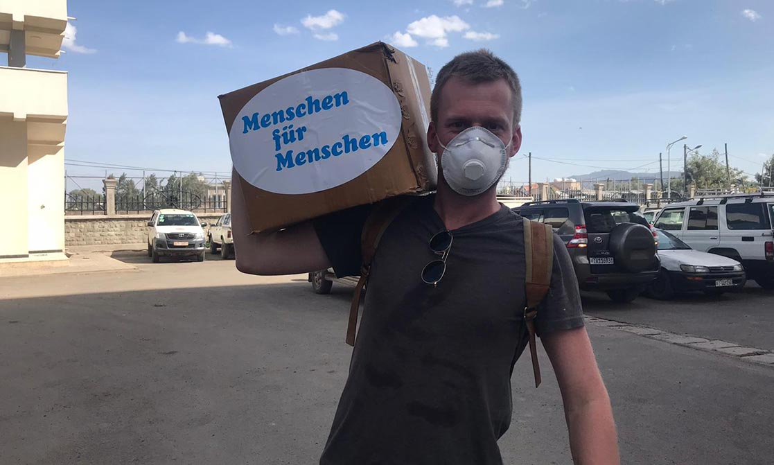 Ein Mann mit Mundschutz trägt eine Kiste.