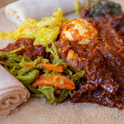 Doro Wot mit Ei und Gemuese auf Injera serviert.