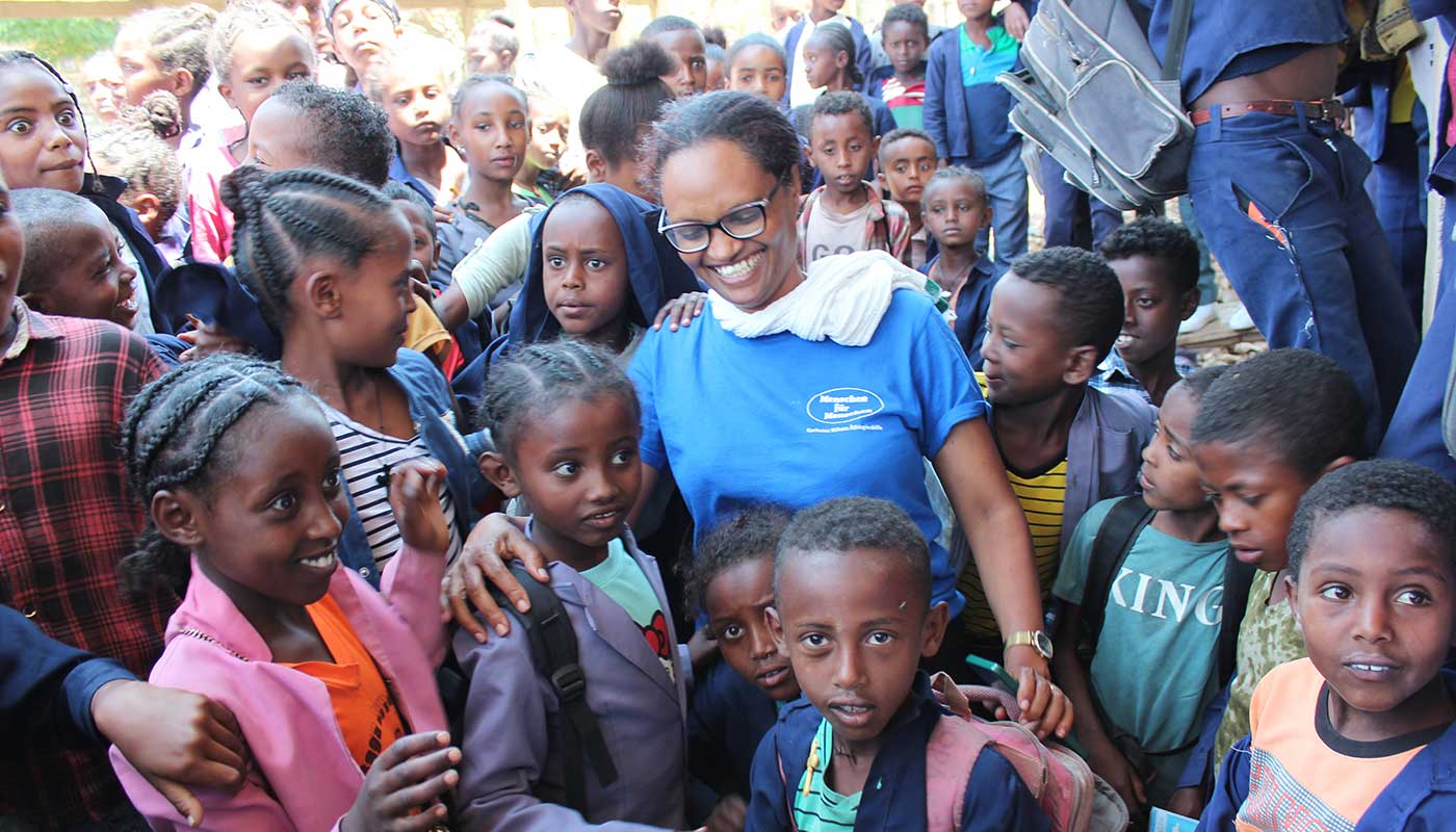 Bahritu Seyoum im blauen Menschen für Menschen-Shirt steht lachend in einer Traube äthiopischer Schülerinnen und Schüler