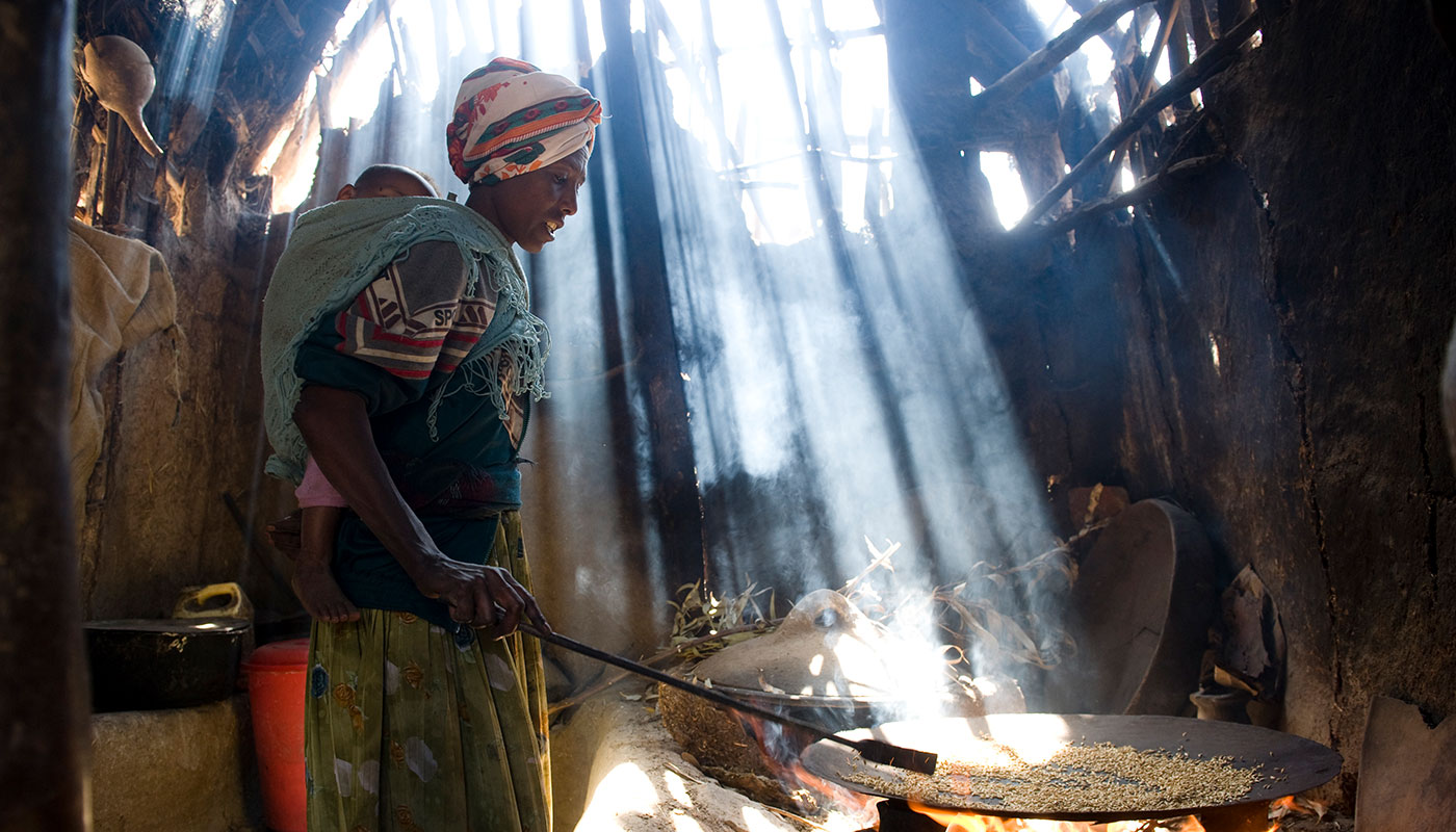 Eine äthiopische Frau trägt ihr Kind am Rücken und röstet Kaffeebohnen im Lichtstrahl in einer Hütte