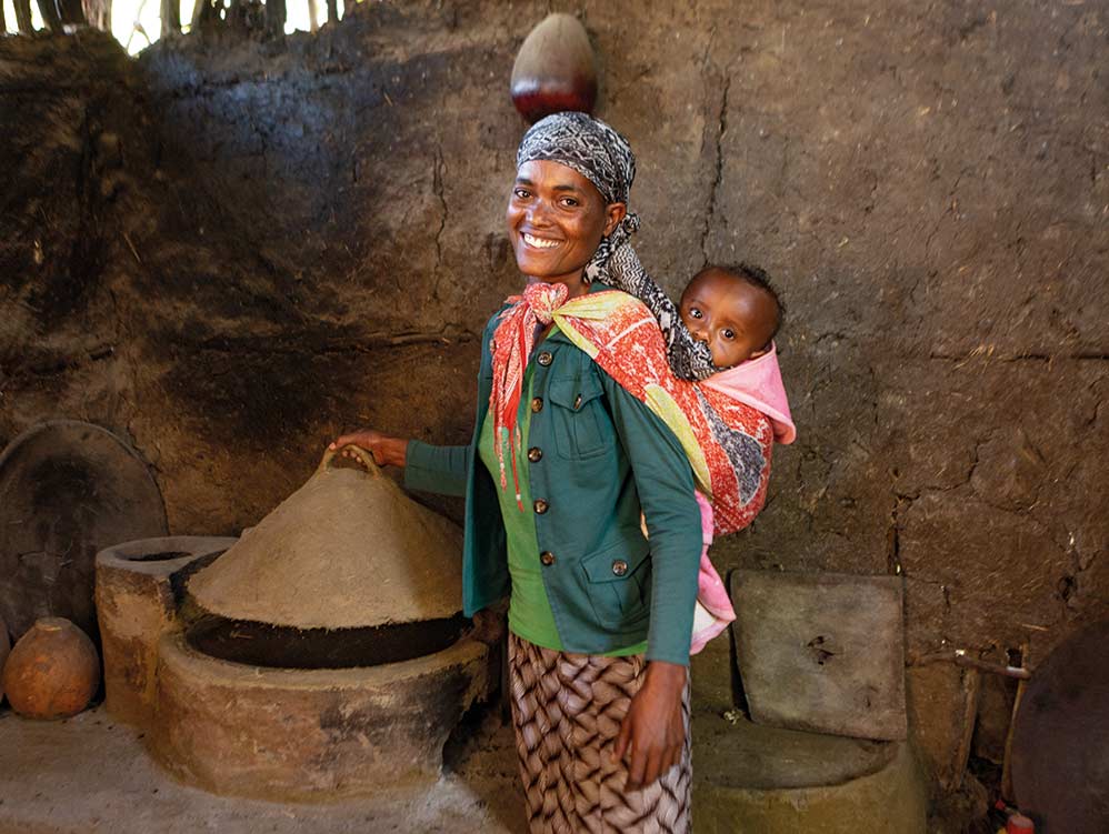 Frau in Äthiopien mit Kind auf ihrem Rücken bei einem holzsparenden Ofen