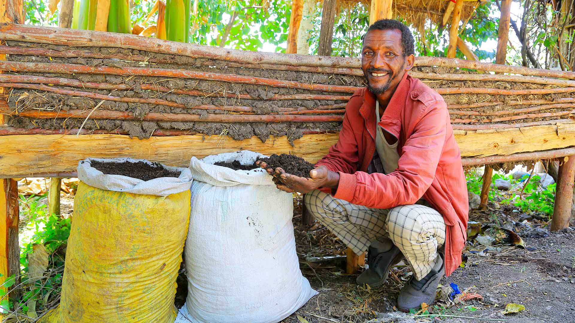 Ein Mann hockt neben zwei Säcken voller Wurmkompost und hält stolz eine Handvoll fruchtbare Erde in die Kamera.