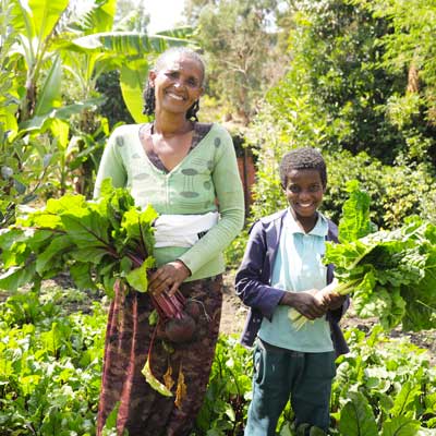 Eine Mutter und ihr Kind stehen im Garten und halten frisch geerntete Rote Bete in den Händen.