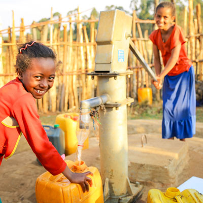 Ein Mädchen zapft klares Wasser aus der Quellfassung.
