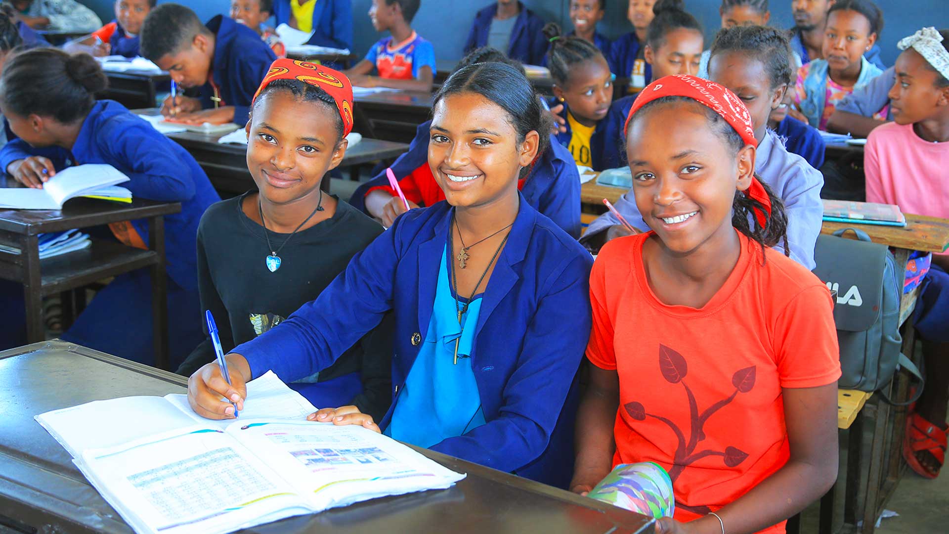 Eine Frau steht mit ihrem Kind auf dem Rücken vor einem Strauch und pflückt Früchte.