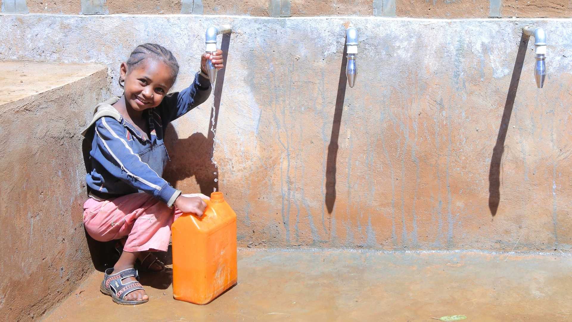 Eine Frau steht mit ihrem Kind auf dem Rücken vor einem Strauch und pflückt Früchte.