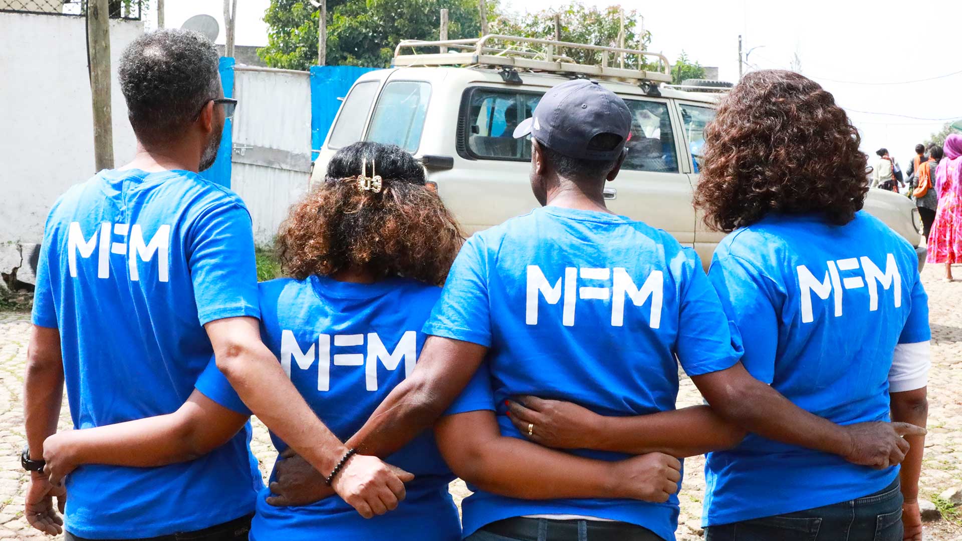Die Mitarbeiter:innen von Menschen für Menschen Äthiopien stehen Arm in Arm zusammen, ihre T-Shirts tragen das Logo von Menschen für Menschen.