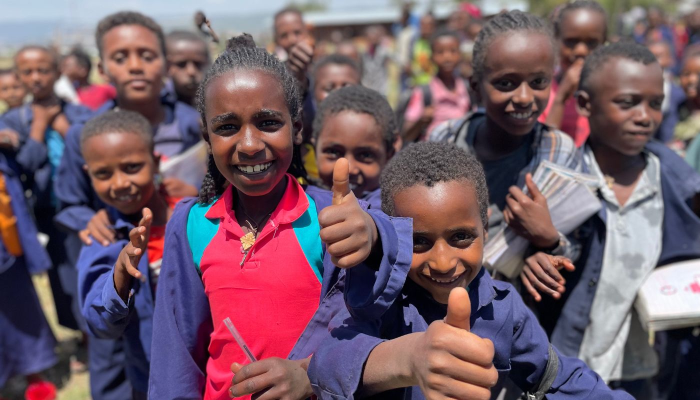 Eine Gruppe äthiopischer Kinder in Schuluniformen. Im Vordergrund ein Mädchen und ein Bub, die den Daumen nach oben heben und lächeln
