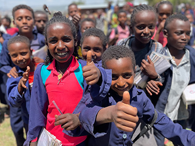 Eine Gruppe äthiopischer Kinder in Schuluniformen. Im Vordergrund ein Mädchen und ein Bub, die den Daumen nach oben heben und lächeln