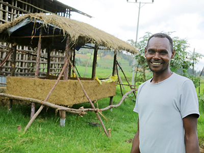 Junger Mann in Äthiopien steht vor einer Wurmkompostierung und lächelt in die Kamera.
