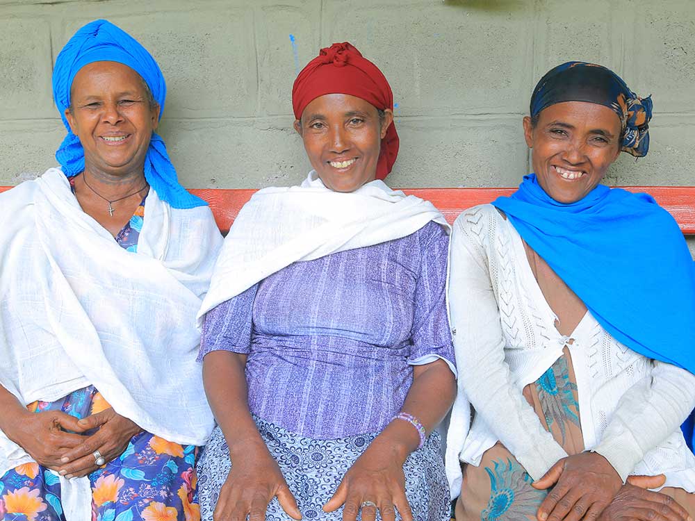 Drei äthiopische Frauen sitzen auf einer Bank und lächeln in die Kamera