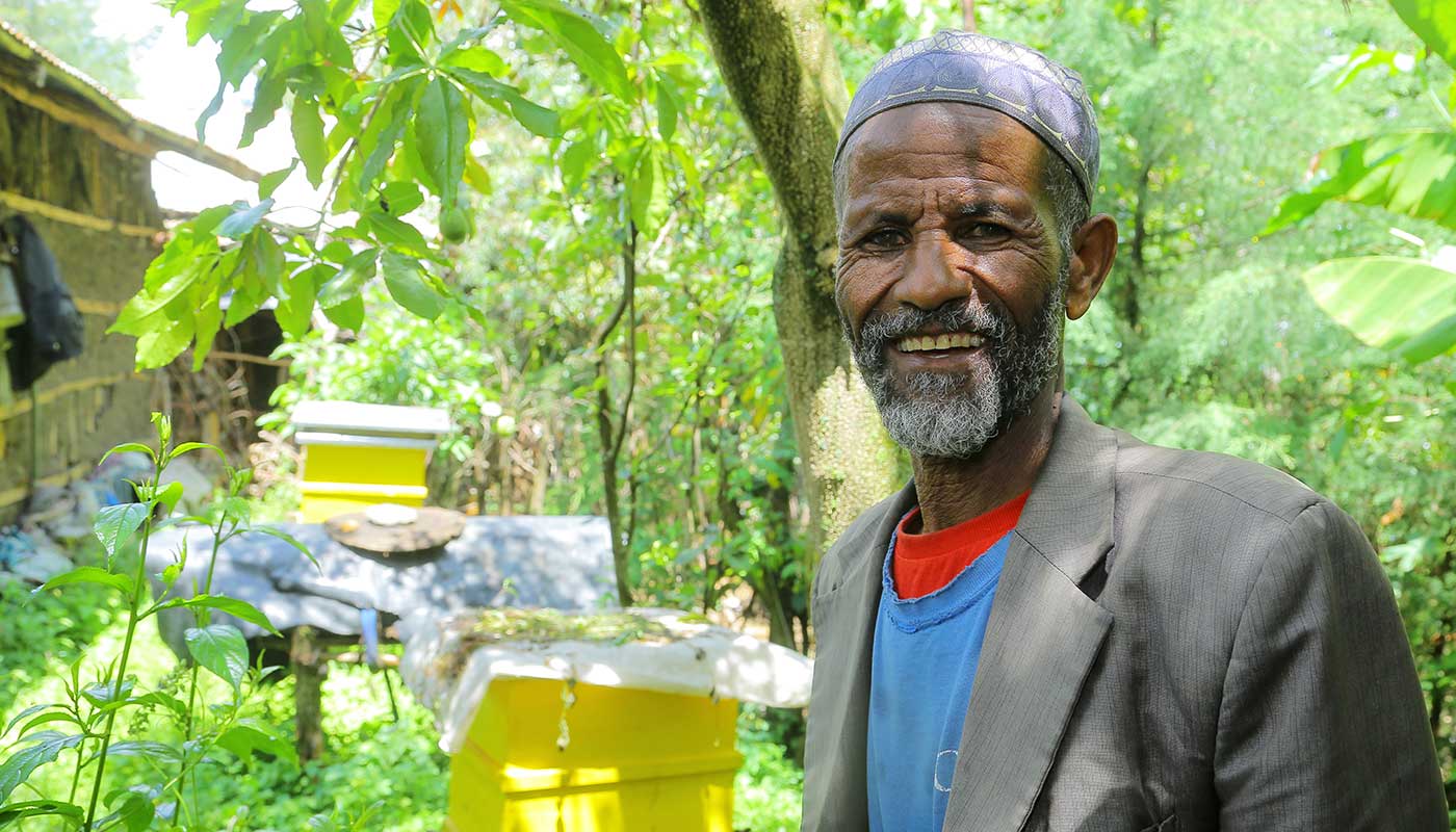 Ein äthiopischer Mann steht vor ein paar Bienenkästen und lächelt in die Kamera