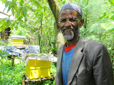 Ein äthiopischer Mann steht vor ein paar Bienenkästen und lächelt in die Kamera