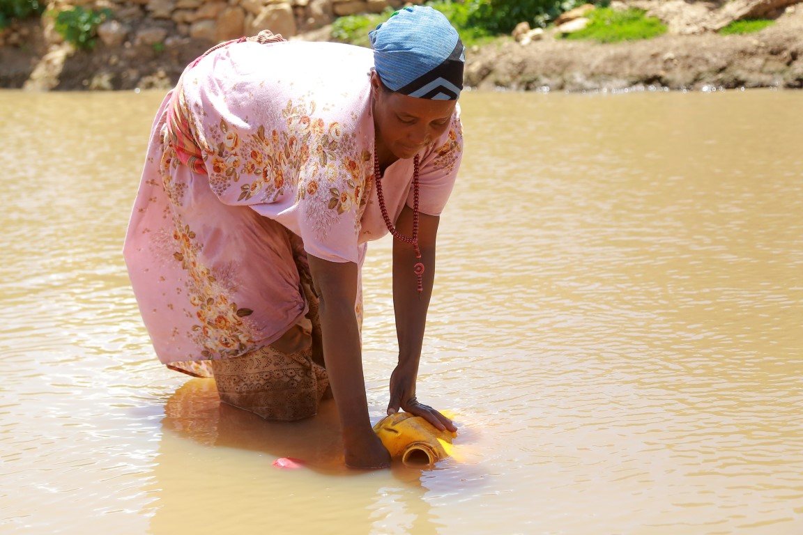 Eine Äthiopierin schöpft Wasser für ihre Familie aus einem trüben Tümpel